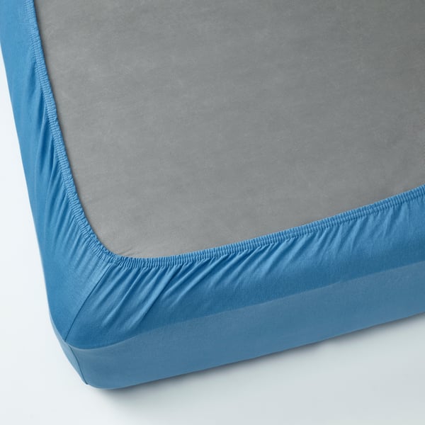 A fitted bedsheet in blue jersey cotton, displaying elastic edges for secure fit.