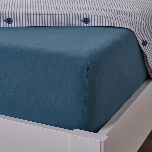 Blue cotton bed sheet on white bed, fitted with elastic, showing corner detail.