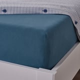 Blue cotton bed sheet on white bed, fitted with elastic, showing corner detail.