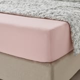 Light pink fitted sheet over beige bedskirt with black vine print bedspread.