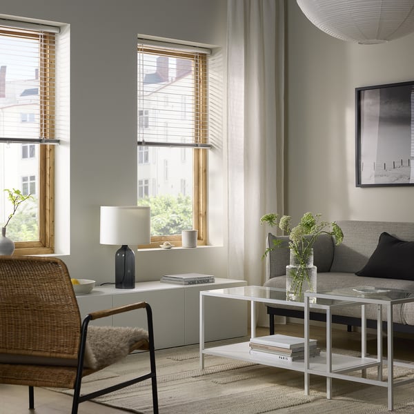 Modern living room with VECKLARFLY blinds, white coffee table, grey sofa, and woven chair. Cozy, contemporary atmosphere.