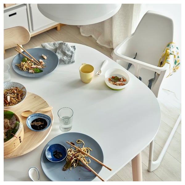 Cozy dining setup with VEDBO table, blue plates, noodles, chopsticks, and partially eaten food. Yellow cup and high-backed chair included.