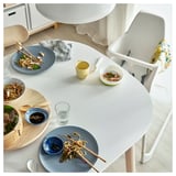 Cozy dining setup with VEDBO table, blue plates, noodles, chopsticks, and partially eaten food. Yellow cup and high-backed chair included.