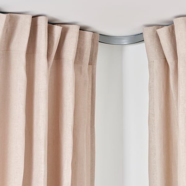 A light-blocking curtain rail with beige curtains, showcasing the VIDGA corner piece designed to deflect curtains around corners.