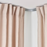A light-blocking curtain rail with beige curtains, showcasing the VIDGA corner piece designed to deflect curtains around corners.