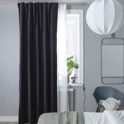 Modern bedroom with black curtains, pendant light, blue chair, plant.