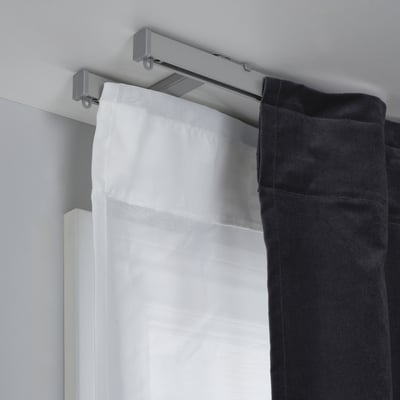 A curtain holder with a metallic track, supporting white sheer and black panel curtains. Its part of the VIDGA system for easy curtain changes.