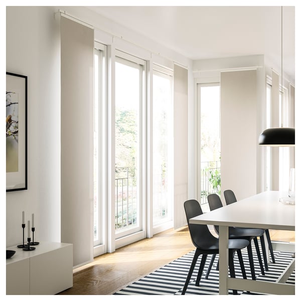 Modern white dining room with large windows and black chairs. Bright light fills the minimalist space with a striped rug.