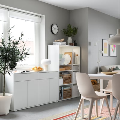 Modern living space featuring VIHALS white storage units, light grey chairs, decorative plants, and colorful rug.