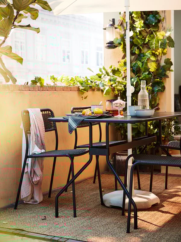 Outdoor patio set with VIHOLMEN black chairs, woven plastic rattan, and metal frame. Surrounded by greenery and dining setup.