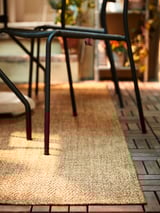 Black VIHOLMEN patio chair legs on beige woven rug.