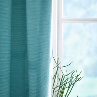 Two light blue curtains hang side by side, floor-length, with a rod pocket top for easy hanging.