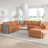 Modern orange l-shaped VIMLE sofa with cushions, centered in a bright, minimalist living room. Large window, white curtains, rug, and coffee table.