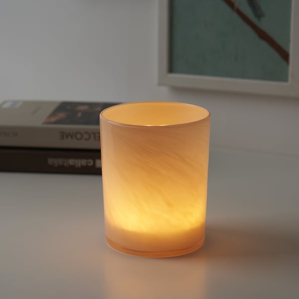 A lit candle in an orange glass holder sits on a table, providing warm light.