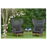 Two gray VINGSÖN outdoor armchairs with high backs on a lawn, surrounded by greenery and white lights.