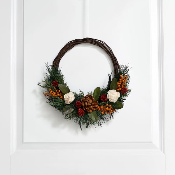 Decorative wreath with pine branches, white roses, and berries hangs on a white wall, adding natural beauty and holiday cheer.