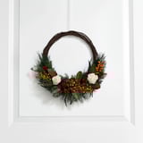 Decorative wreath with pine branches, white roses, and berries hangs on a white wall, adding natural beauty and holiday cheer.
