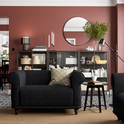 Cozy dark grey armchair in stylish living room with red walls and black shelves.