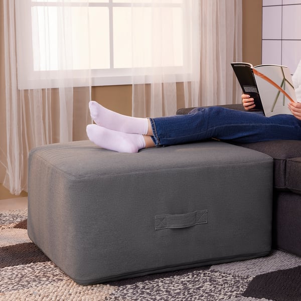 Comfy grey VITHÄLL ottoman under feet, beside reader on sofa. Soft, square with handle.