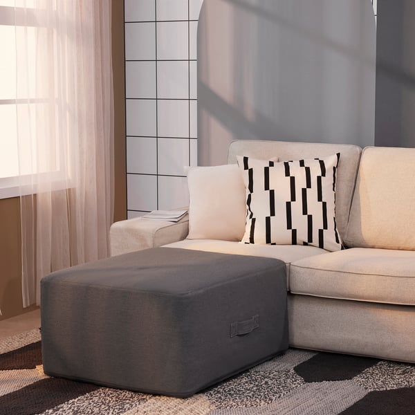 Modern living room with beige sectional couch, gray ottoman, and patterned pillows.