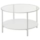 Option: A VITTSJÖ coffee table, white, with a round shape and a clear glass top. It has a metal frame and a bottom shelf for storage.