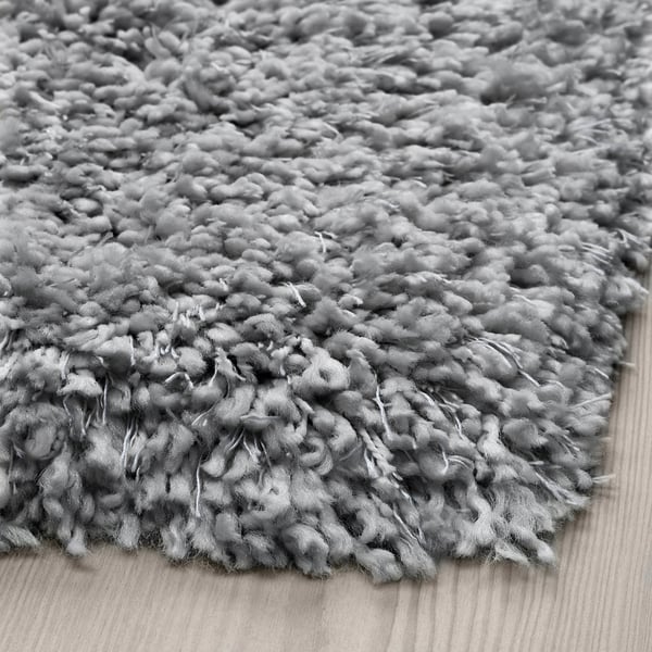 Close-up of a shaggy, gray rug with thick, varied texture on a wooden floor.