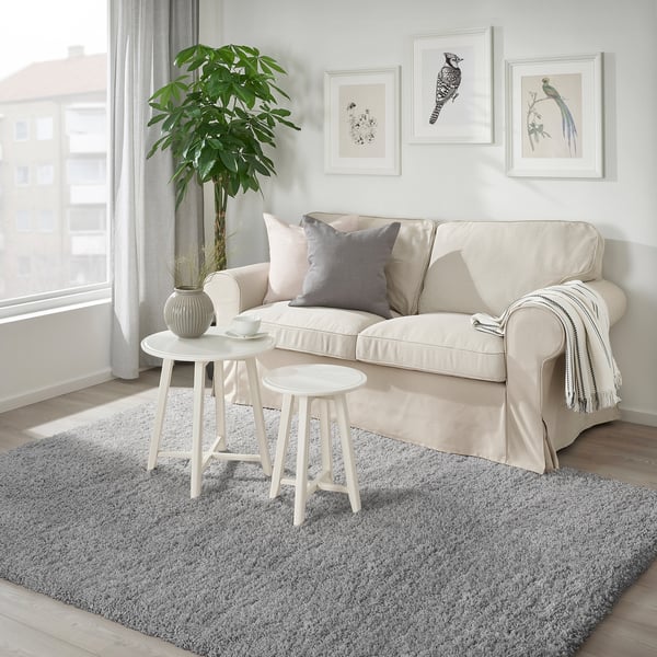 Modern living room with grey rug, side table, stool, and beige couch. Soft, cozy, and spacious.
