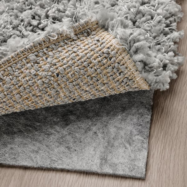 Exhibitory view of thick, shaggy gray rug with visible backing, highlighting its texture and comfort.