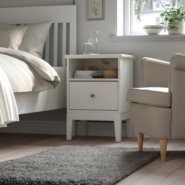 Bedroom with VOLLERSLEV rug, white bed, nightstand, beige chair.