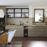 Modern kitchen VOXTORP high-gloss, dark grey-brown cabinet doors with sleek integrated handles, wooden chair, tiled floors, and metallic appliances.