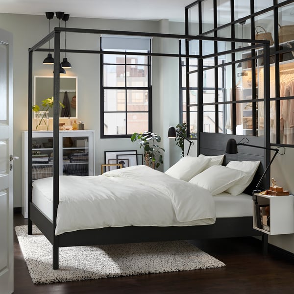 Modern black four-poster bed, centered rug, white bedding, large windows.
