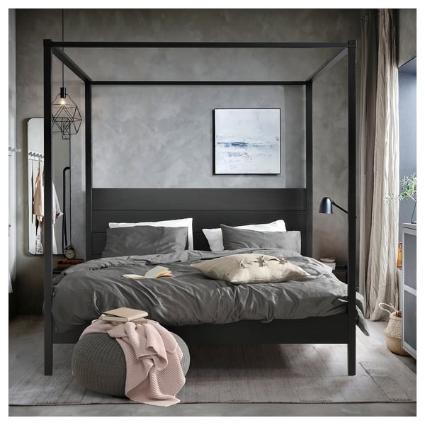 Modern grey four-poster bed with dark wood frame, white and grey bedding, art, and chic decor.