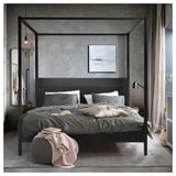 Modern grey four-poster bed with dark wood frame, white and grey bedding, art, and chic decor.