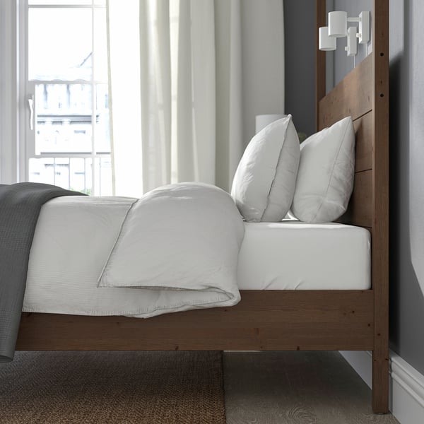 Bed with wooden headboard, white pillows, sunlight through large windows.