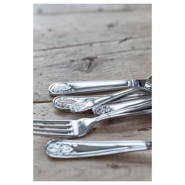 Sølvbestik sat på træbord. Inkluderer gaffel, kniv og ske med indviklede blomsterdesigns, skinnende rustfrit stål.