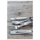Sølvbestik sat på træbord. Inkluderer gaffel, kniv og ske med indviklede blomsterdesigns, skinnende rustfrit stål.
