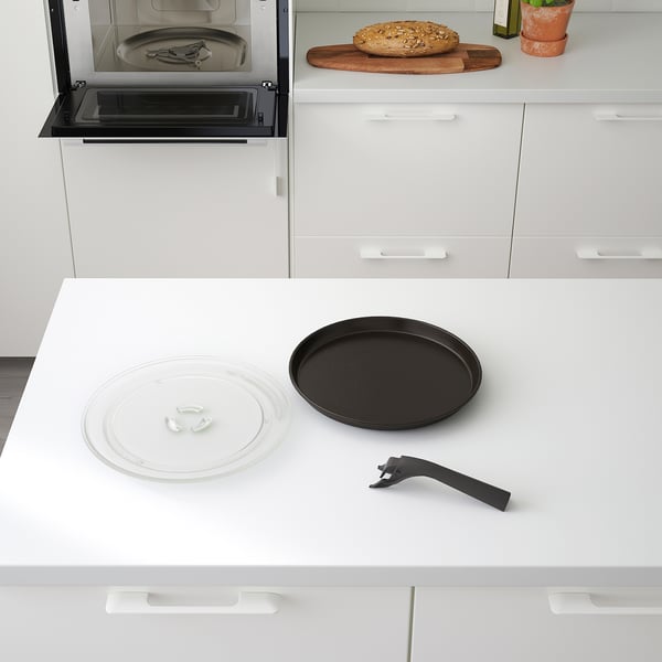 Moderne køkkenscene med indbygget mikrobølgeovn med crisp-plade, drejeskive og værktøj sammen med bordplade med brød.