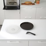 Moderne køkkenscene med indbygget mikrobølgeovn med crisp-plade, drejeskive og værktøj sammen med bordplade med brød.