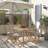 Udendørs spisebordssæt i træ med lyst bord, grå polstrede stole, planter og paraply.
