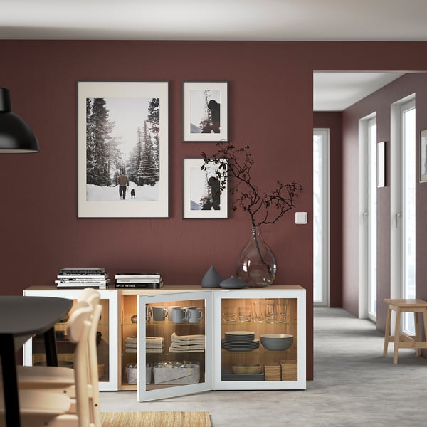 BESTÅ skænk med glaslåger med opvask. Tre fotos på bordeauxvæg. Justerbare hylder og stilfuld vase med grene.