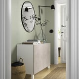 Hvid marmor BESTÅ skænk mod grøn væg med bøger, vase, spejl og lampe.