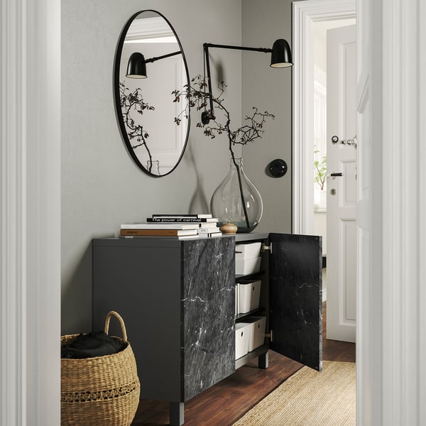 Sort BESTÅ opbevaringsmøbel med åbne døre, der afslører kasser, designet med bøger, en vase og et spejl ovenover.
