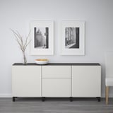 Hvid skænk med opbevaringsskuffer og hylder. To indrammede sort/hvide fotos ovenfor. Skål og vase på toppen.