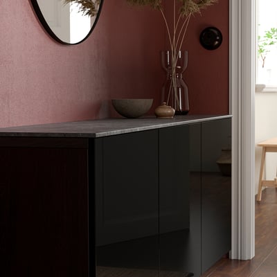 Moderne sort BESTÅ-disk med grå marmor, vase, skål og spejl mod rødbrun væg.