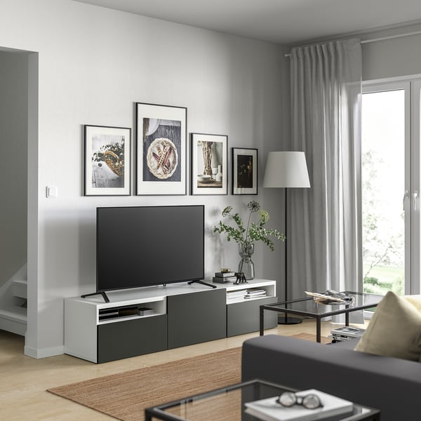 Moderne opholdsstue med BESTÅ-tv-bord, fladskærms-tv og indretning. Stort vindue, tæppe, sofabord med bøger, sort sofa, beige pude.