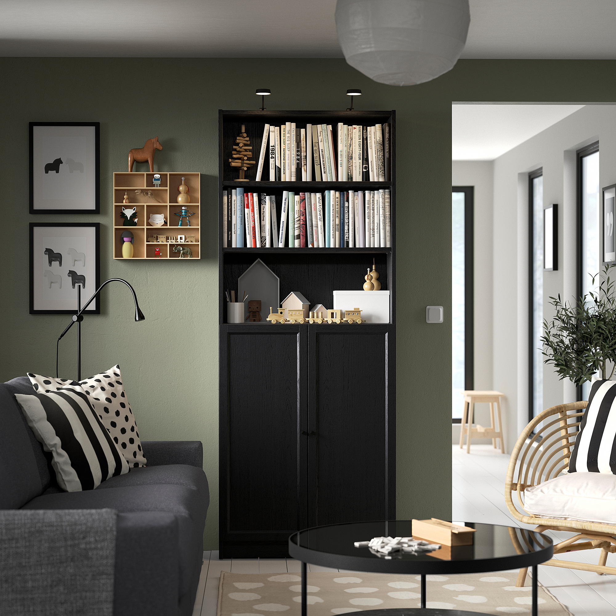 Moderne stue med grå sofa, sort BILLY reol fyldt med bøger, pyntegenstande og print på olivengrøn væg.