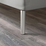 Moderne seng med slanke, metalliske ben på stilfuldt trægulv.