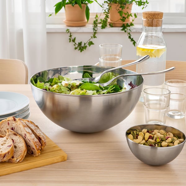 Stor skål i rustfrit stål med salat, tang, brød, nødder, glas og vandkande på et træbord.