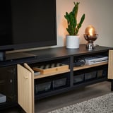 Moderne tv-stativ med glasdøre, åbent rum med skaksæt, anlæg og lampe. Sort og træ combo, stilfuld og organiseret.