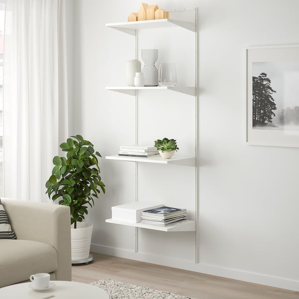 Hvid BOAXEL reol, minimalistisk design, med bøger, vaser og en plante ved siden af en cremefarvet sofa og et stort vindue.